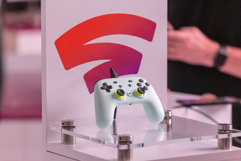 Photo of a Google Stadia controller sat atop a clear pedestal with the Stadia logo behind it