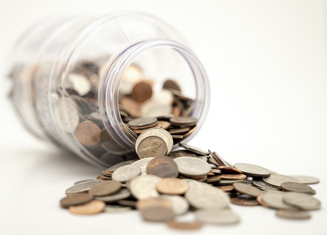 Image of some coins spilling out onto a white table from inside a jar 