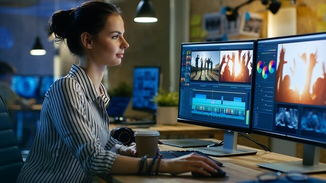 Photo of a woman sat at an office PC setup editing a video 