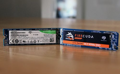 Close up photo of a Seagate FireCuda and BarraCuda NVMe SSD stood upright next to each other on a wooden table