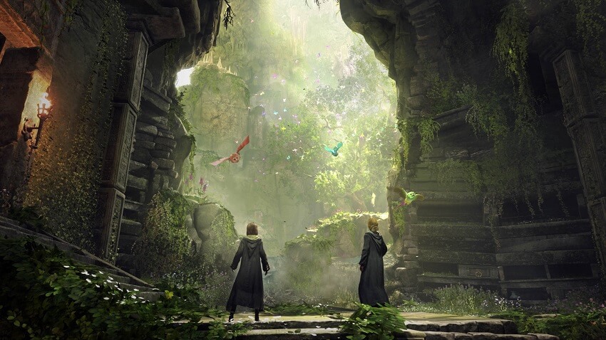 Game capture image from Hogwarts Legacy showing two witches stood at a large opening in a rock wall through which is a bright fantastical looking forest environment