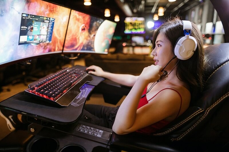 Image of a girl sat in a PC gaming chair with 2 monitors and a keyboard and mouse in front of her