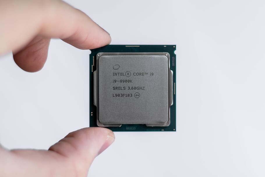 Close up of a finger and thumb holding an Intel Core i9-9900K CPU against a white background