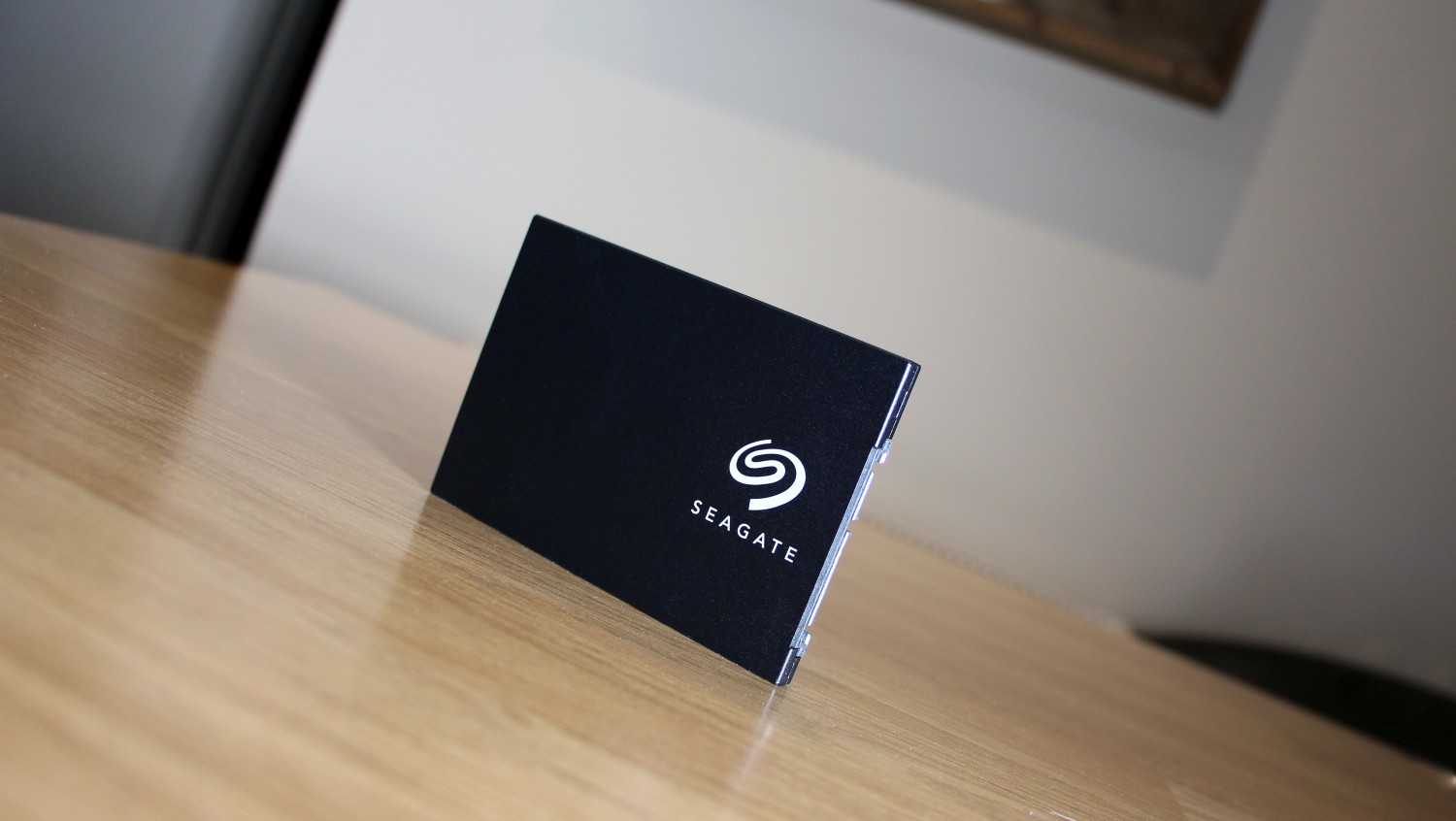 Photo of a Seagate BarraCuda SSD stood upright on a desk, with the white Seagate logo on the front