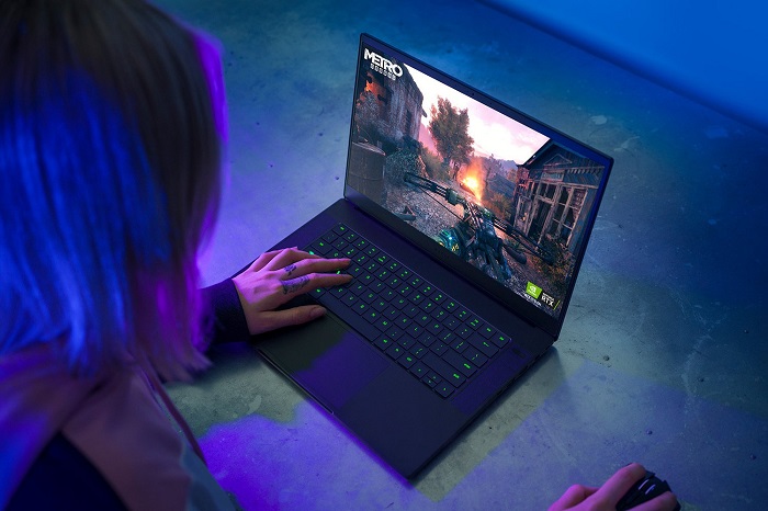 Promotional image for a Razer gaming laptop, sitting open on a concrete surface whilst a woman plays Metro Exodus on it