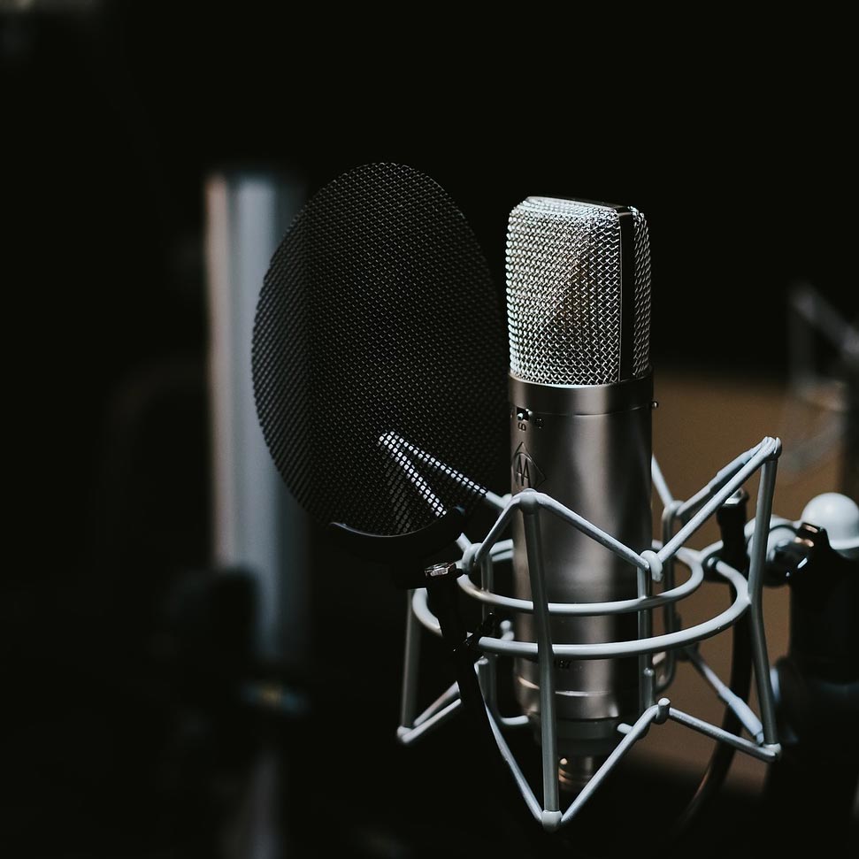 Image of a silver studio microphone with a pop shield in front of it
